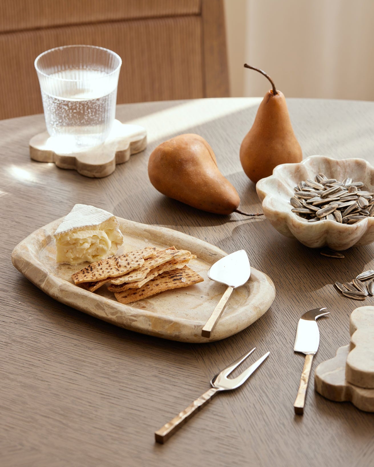 Table setting with cheese, crackers, pears, and utensils on a wooden table.