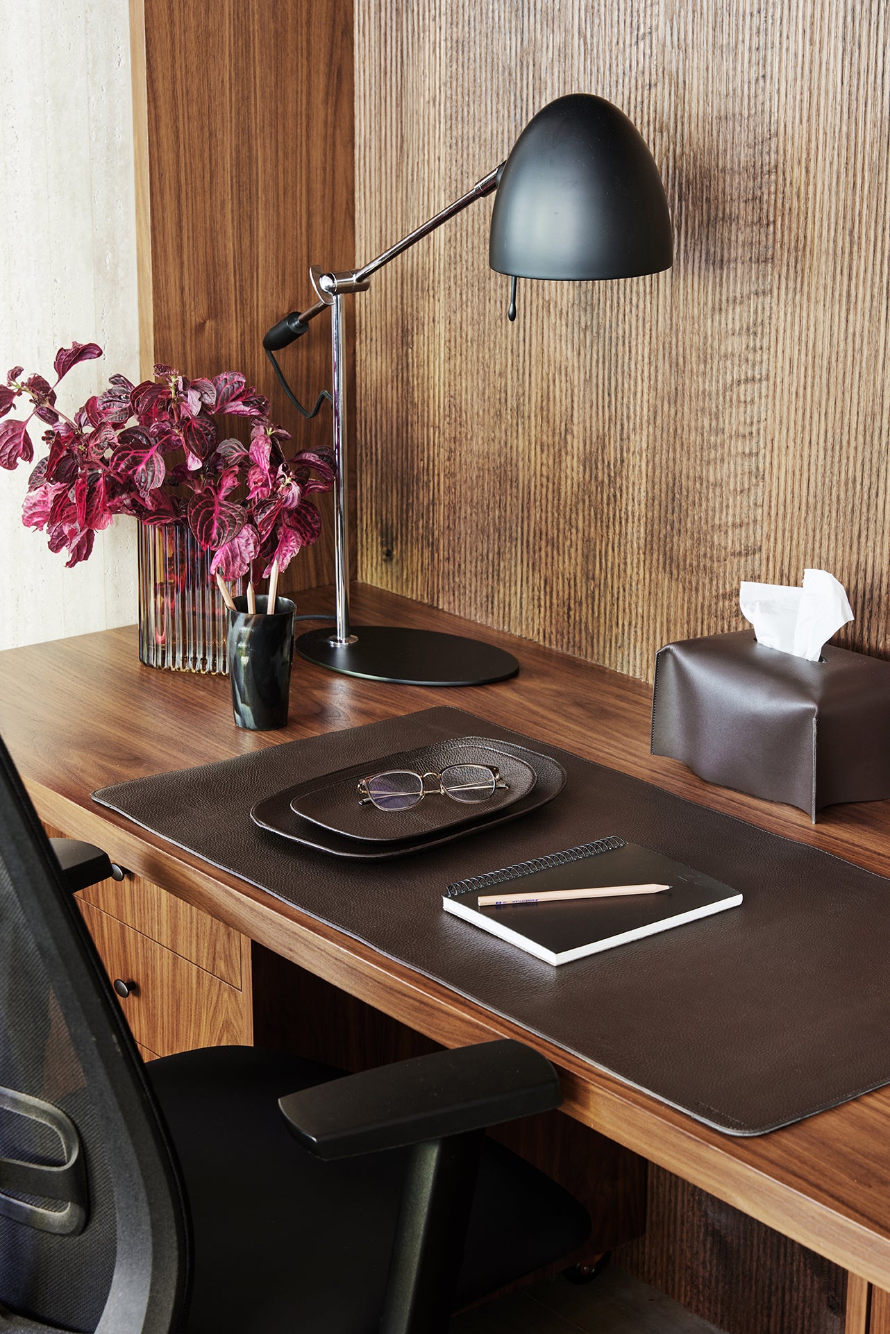 Wooden desk with black lamp, tablet, glasses, and flowers in a room with wooden walls.