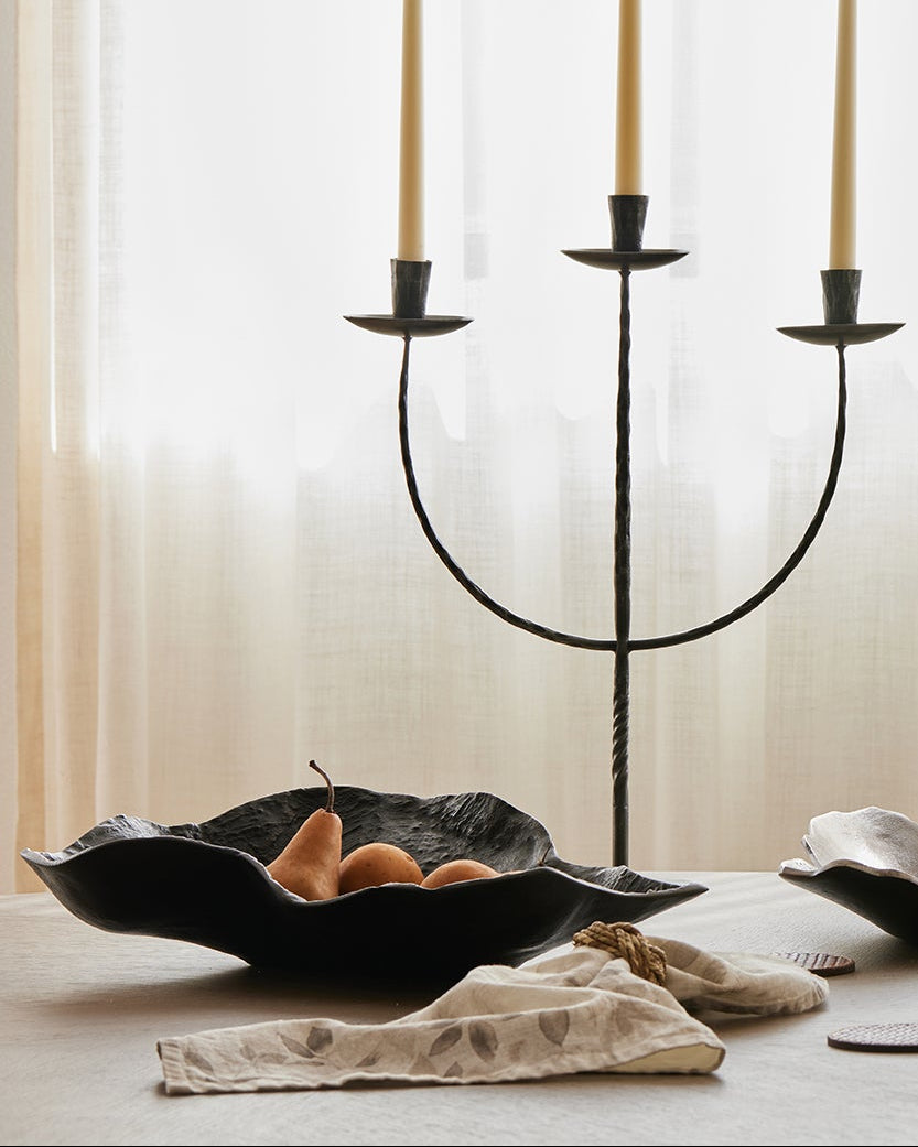 Decorative setup with a black candelabra, vase with greenery, and bowls on a table.
