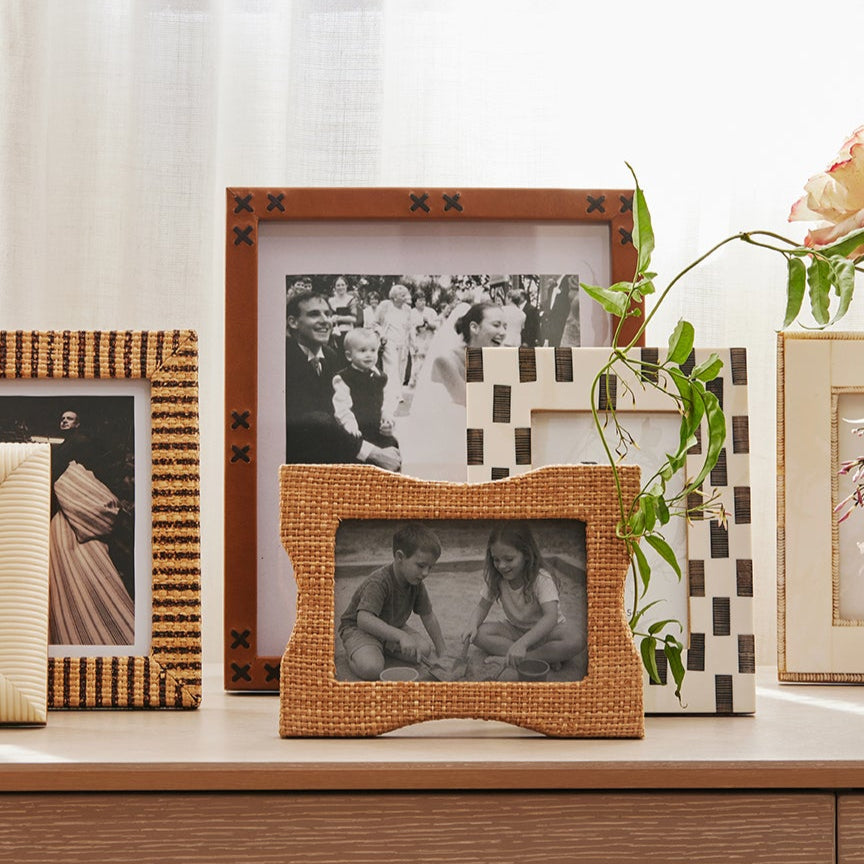 Collection of framed photographs and a vase with flowers on a wooden surface.
