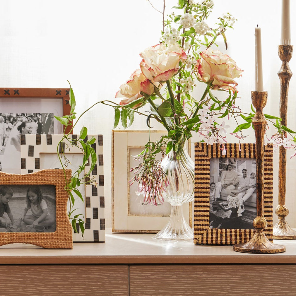 Collection of framed photographs and a vase with flowers on a wooden surface.