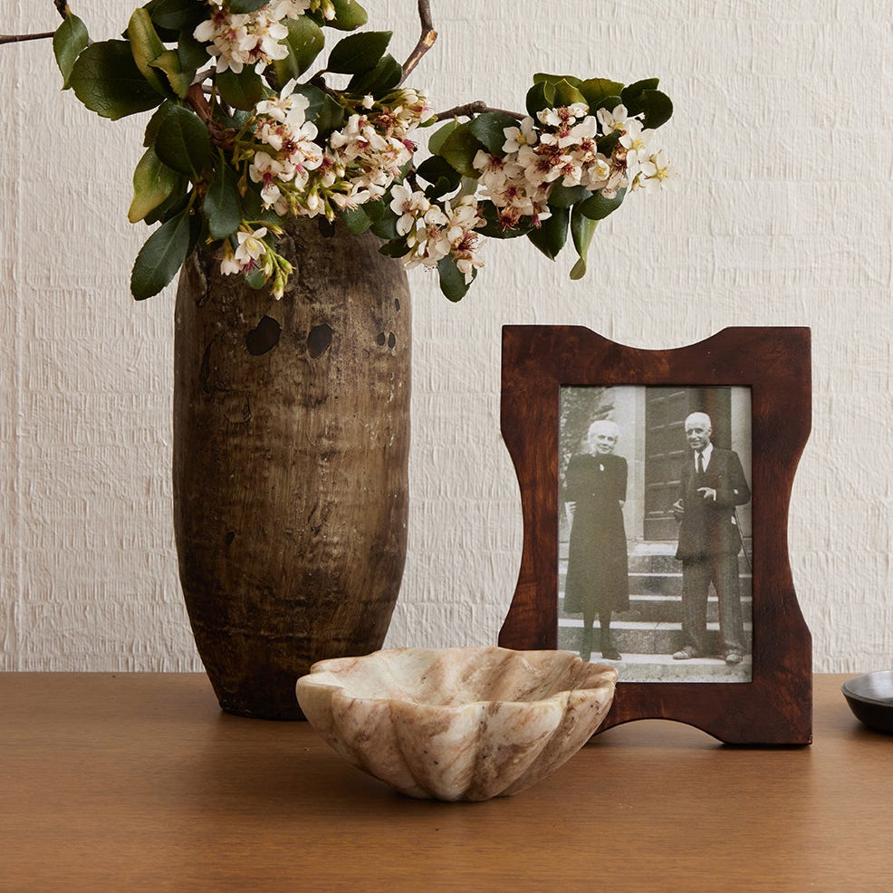 Decorative items on a wooden surface including a vase with flowers, a photo frame, a bowl, and a candlestick.