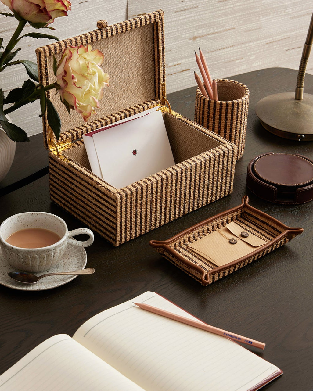 Decorative desk setup with a photo frame, tea set, and stationery items on a wooden surface.