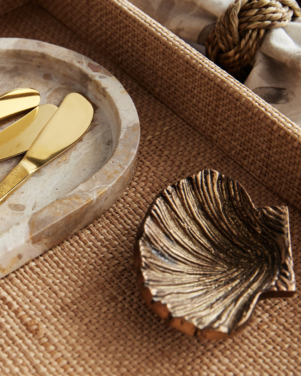 Set of gold pate knives on a stone tray with a shell decorative item.