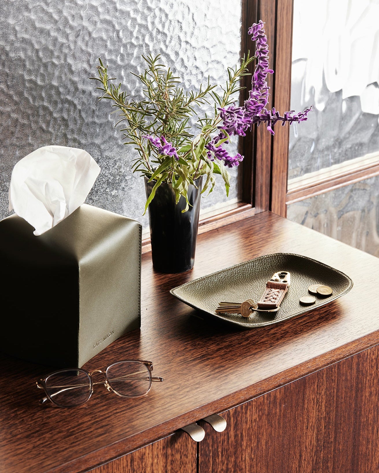 Decorative setup on a wooden surface with a vase of flowers, tissue box, and small items.