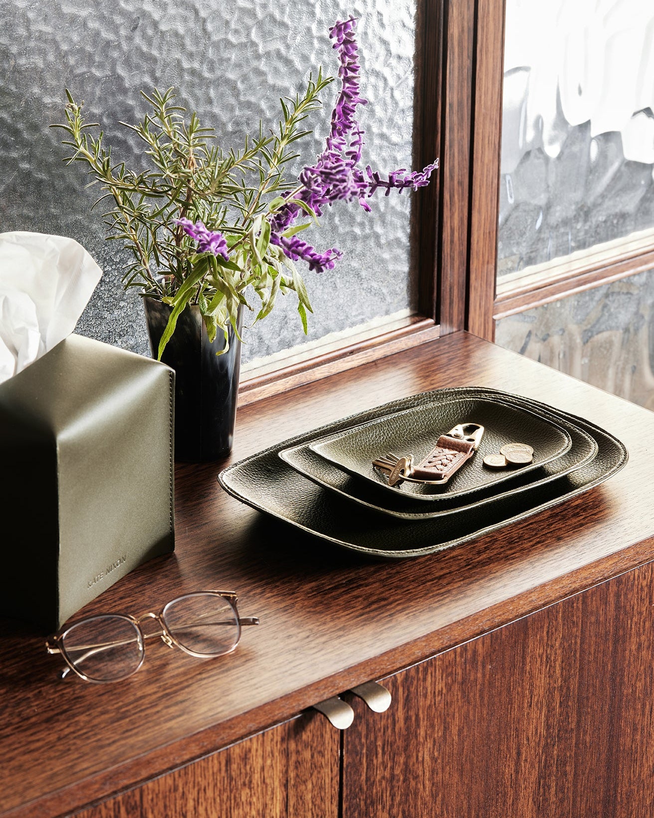 Decorative setting with a vase of flowers, glasses, and a tray on a wooden surface.