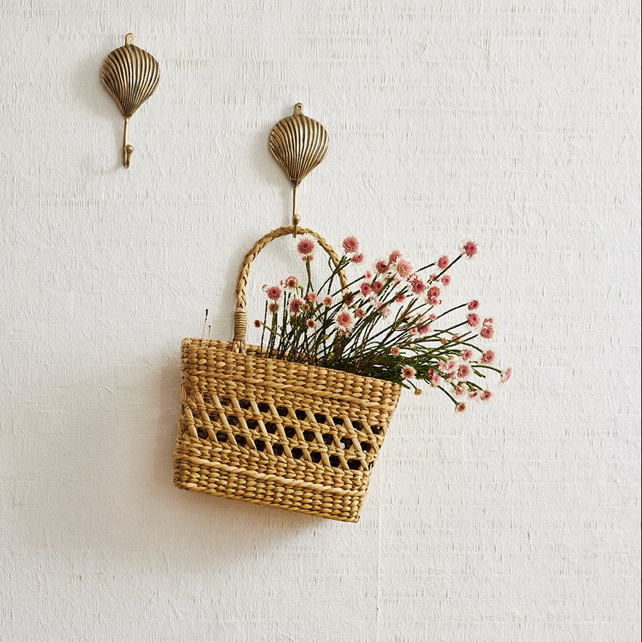 Wooden chair with white cushion next to a wooden side table with candles and a basket of flowers on a light gray wall.
