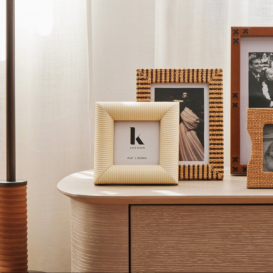 Collection of framed photographs and a vase with flowers on a wooden surface.