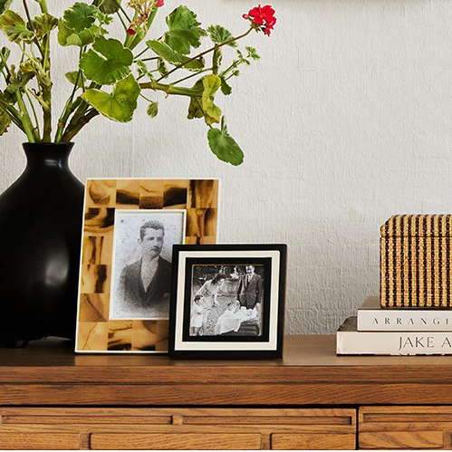 Decorative setup with framed photos, a vase of flowers, books, and small sculptures on a wooden surface.