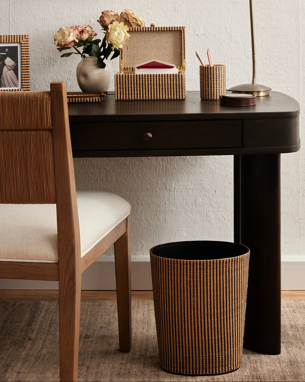 Small black desk with wooden chair, decorative items, and a lamp in a room setting.