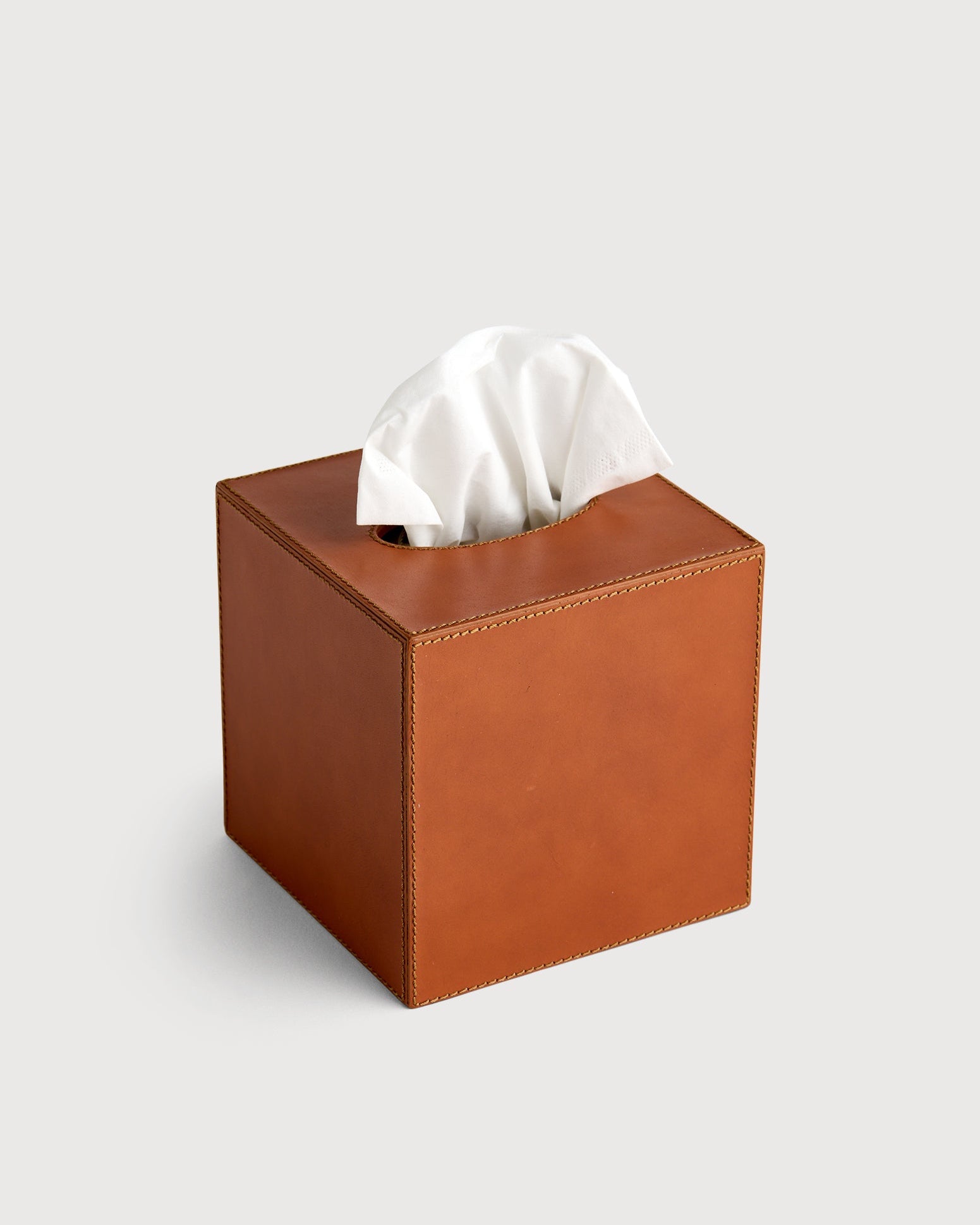 Brown leather tissue box with white tissues on a light gray background